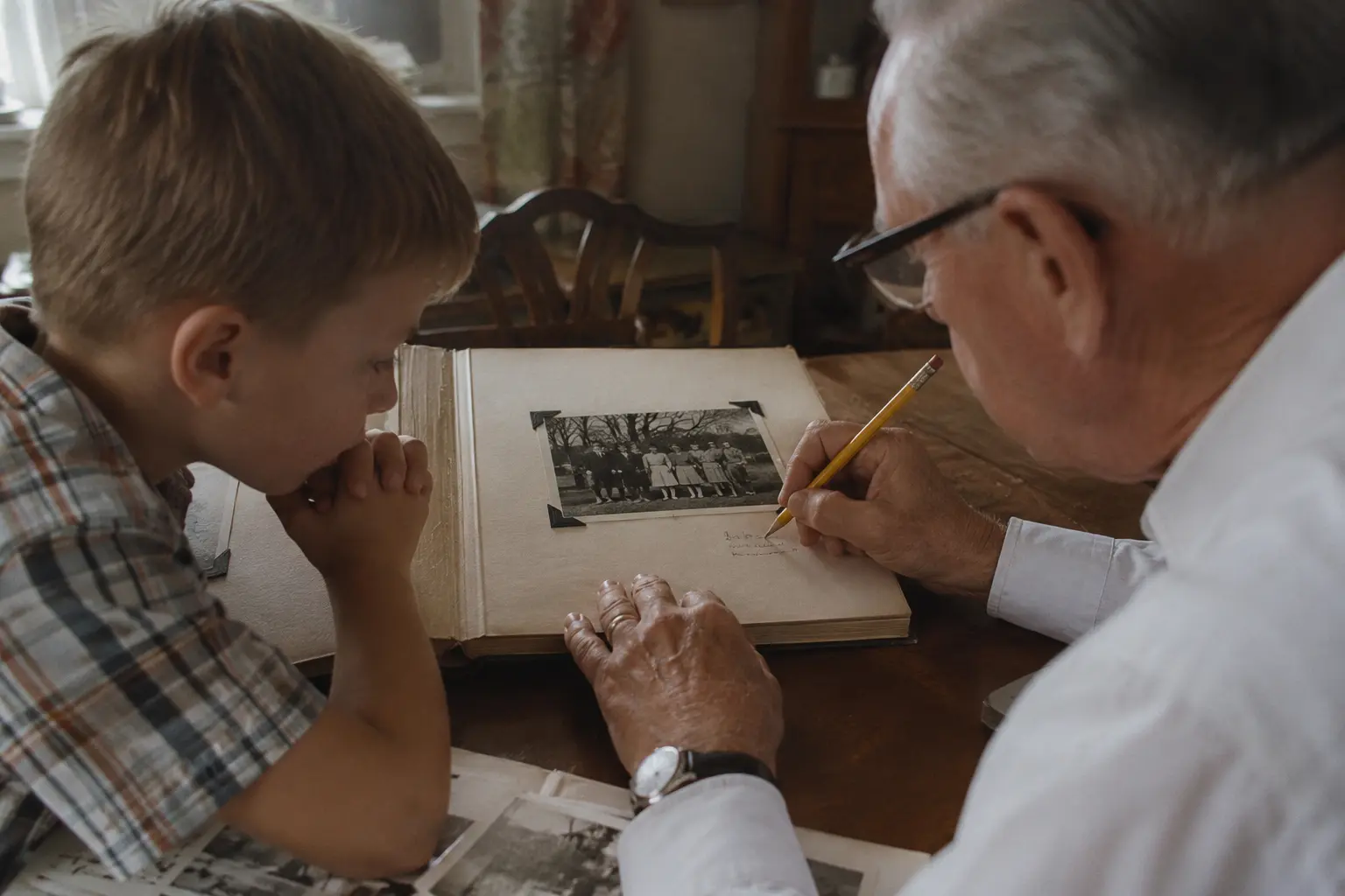 An older relative writing a caption beneath a mounted family photograph while a child watches