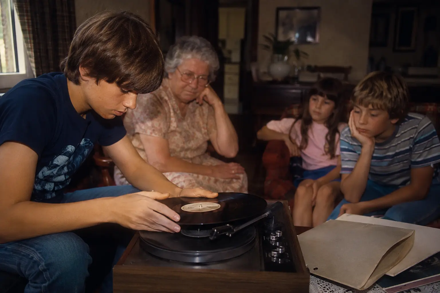 A teenager flipping a vinyl record while siblings and a grandparent wait in an early 1980s family room