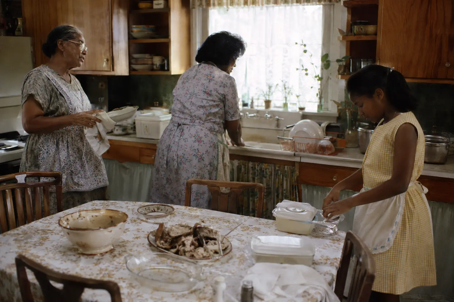 Three generations cleaning a 1960s kitchen and packing leftovers after Sunday dinner