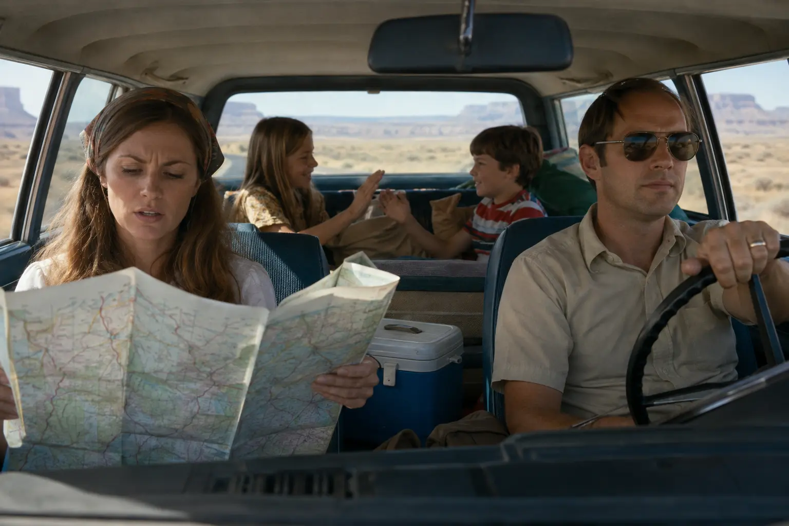 A passenger unfolding a large paper road map inside a family car