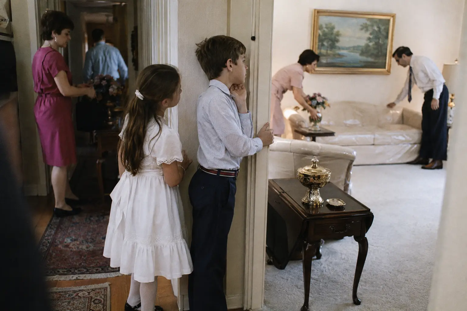 Children watching as adults prepare a spotless 1970s formal living room for guests